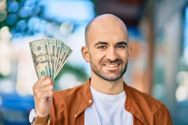 Young hispanic bald man smiling happy holding usa dollars at the city.