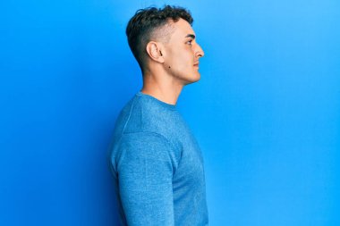 Hispanik genç adam, günlük kışlık süveter giyiyor. Tarafını arıyor, profil pozu veriyor. Doğal bir yüzü ve kendine güvenen bir gülümsemesi var.. 