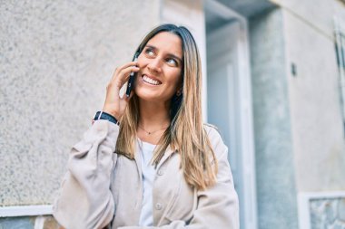 Beyaz kadın gülümsüyor. Şehirdeki akıllı telefondan konuşuyor..
