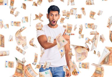 Gündelik kıyafetler giyen genç latin adam parmaklarını yana doğru göstererek şaşırdı, ağzı açık hayret içinde kaldı..