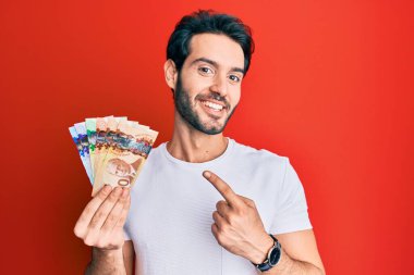 Kanadalı dolarları tutan İspanyol genç adam mutlu bir şekilde elini ve parmağını gösterdi. 