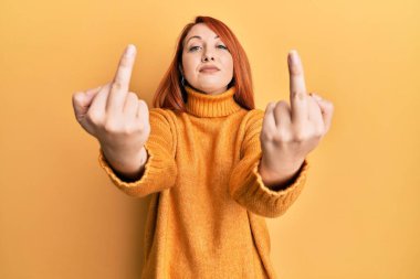 Güzel kızıl saçlı kadın orta parmağını gösteriyor. Kötü hareket ediyor. Yüzünde ciddi bir ifadeyle rahatlamış. Basit ve doğal bir şekilde kameraya bakıyorsun.. 