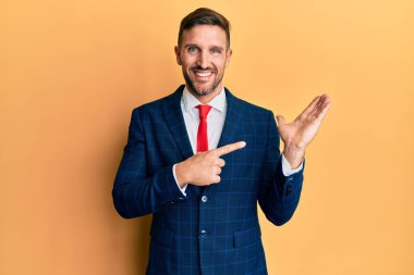 Sakallı, takım elbiseli ve kravatlı yakışıklı bir adam kameraya hayret ediyor ve gülümsüyor.. 