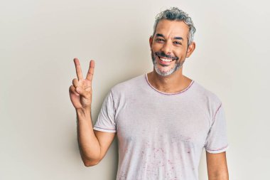 Orta yaşlı, gri saçlı, günlük kıyafetler giyen, iki numaralı parmaklarıyla işaret eden, kendinden emin ve mutlu bir adam.. 