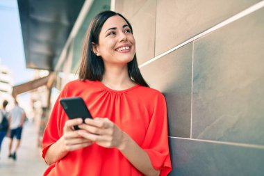 Genç Latin kız şehirde akıllı telefon kullanarak mutlu bir şekilde gülümsüyor..