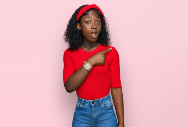 Gündelik giysiler giyen güzel Afrikalı genç bir kadın parmaklarını yana doğru göstererek şaşırdı, ağzı açık hayret içinde kaldı.. 