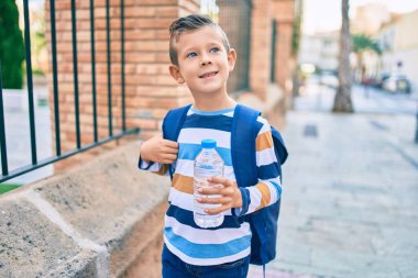 Sevimli beyaz çocuk gülümsüyor. Şehirde elinde bir şişe su tutuyor..