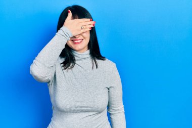 Gündelik kıyafetler giyen, gülümseyen ve gülümseyen genç İspanyol kadın şaşırmak için gözlerini kapatıyor. kör kavram. 