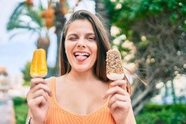 Genç ortadoğulu kız dil ısırıyor ve şehirde dondurma tutuyor..