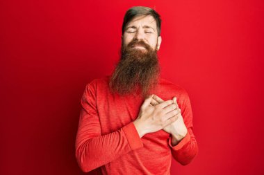 Uzun sakallı, sıradan kıyafetler giyen, göğsünde elleriyle gülümseyen, yüzünde minnet ifadesi olan kızıl saçlı bir adam. sağlık kavramı. 