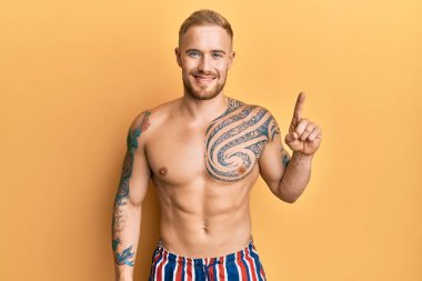 Mayo giyen genç, beyaz bir adam bir numaralı parmağını gösterip gülümserken kendinden emin ve mutlu.. 