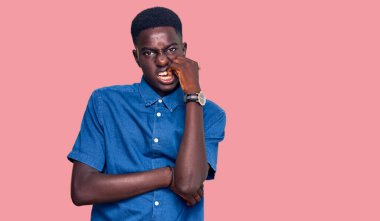 Gündelik kıyafetler giyen genç Afro-Amerikan bir adam gergin görünüyor ve elleri ağzında tırnak yiyor. anksiyete. 