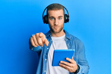 Kulaklık takmış, kamerayı işaret eden genç beyaz bir adam. Kendine güvenen ve ciddi görünen bir jest. 