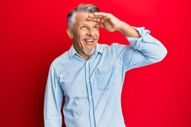 Orta yaşlı, gri saçlı, günlük kıyafetler giyen mutlu ve tebessüm eden bir adam. arama kavramı. 