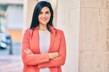 Kollarını kavuşturup gülümseyen genç ve güzel bir iş kadını şehirde mutlu bir şekilde duruyor..