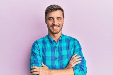 Sıradan giyinen yakışıklı beyaz adam kollarını kavuşturup kameraya bakarken gülümsüyor. pozitif kişi. 