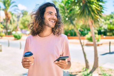 Genç İspanyol adam mutlu bir şekilde gülümsüyor. Akıllı telefon kullanıyor ve şehirde kahve içiyor..