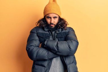 Gündelik kışlık kıyafetler giyen genç Arap adam kuşkucu ve gergin, yüzünde çapraz kollu tasvip etmeyen ifade. negatif kişi. 