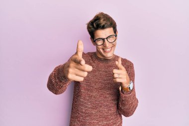 Sıradan süveter giyen ve gözlüklü yakışıklı beyaz adam kamerayı mutlu ve komik yüzüyle işaret ediyor. iyi enerji ve titreşimler. 