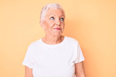 Son sınıf güzeli, mavi gözlü, gri saçlı, sarı arka planda klasik beyaz tişört giyen, gülümseyen ve başka yöne bakan güzel bir kadın.. 