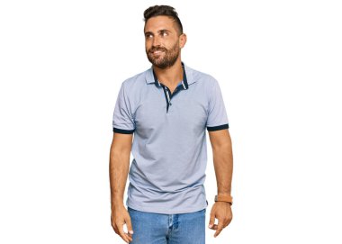 Sakallı, sıradan giyinmiş, gülümseyen, yan tarafa bakıp düşünen yakışıklı bir adam.. 