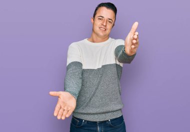 Sıradan bir kazak giyen yakışıklı genç adam kucaklanmak için kollarını açmış kameraya bakıyor. Mutluluğu kucaklayan neşeli bir ifade.. 