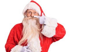 Geleneksel Noel Baba kostümü giyen gri saçlı ve uzun sakallı yaşlı bir adam. Parmak omuza ve burunla işaret ediyor. Neşeli gülümsüyor. güzellik konsepti 