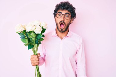 Kıvırcık saçlı ve elinde bir buket beyaz çiçek tutan yakışıklı genç adam. Şaşırmak için ağzı açık ve korkmuş, inançsız bir yüz. 