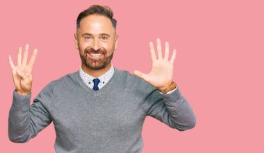 İş kıyafetleri giymiş yakışıklı orta yaşlı bir adam dokuz numarayı gösterip işaret ederken kendine güvenen ve mutlu bir şekilde gülümsüyor.. 