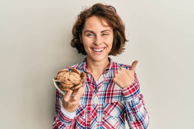 Çikolata parçacıklı kurabiyeler taşıyan genç esmer kadın mutlu ve pozitif gülümsüyor, başparmağı mükemmel ve onay işareti yapıyor. 