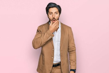 İş kıyafetleri giyen genç İspanyol adam, elleri çenesinde olan inançsızlıktan, şaşkınlıktan ve şaşkınlıktan büyülenmiş görünüyor. 