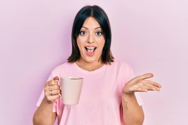 Bir fincan kahve içen genç İspanyol kadın başarıyı mutlu bir gülümsemeyle ve kazanan yüz ifadesiyle kutluyor. 