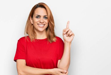 Yüzünde kocaman bir gülümseme olan gündelik kırmızı tişört giyen İspanyol genç kadın kameraya el ve parmak ile bakıyor.. 