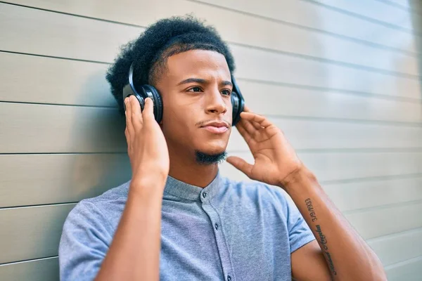 Young african american man with unhappy expression listening to music using headphones at the city.