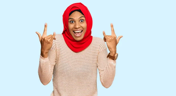 身穿传统的伊斯兰头巾的年轻的非洲裔美国女人带着疯狂的表情高举双手做岩石符号 音乐明星 重音乐概念 — 图库照片