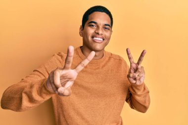 Kış süveteri giyen genç, yakışıklı İspanyol adam kameraya bakıp zafer işareti yapıyor. İki numara.. 