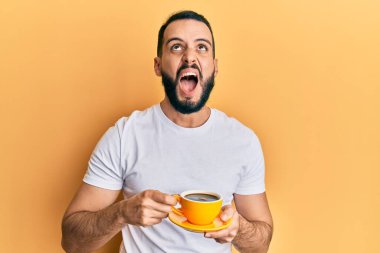Sakallı genç adam bir fincan kahve içiyor kızgın ve deli gibi bağırıyor sinirli ve öfkeli, öfkeyle bağırıyor.. 