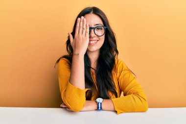 Güzel, esmer, gözlüklü, sıradan elbiseli bir kadın masanın üzerinde oturuyor bir gözünü eliyle kapatıyor, yüzünde kendine güvenen bir gülümseme ve sürpriz bir duygu var.. 