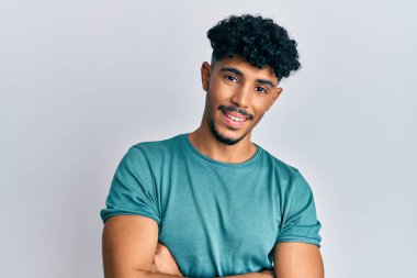 Genç Arap yakışıklı sıradan kıyafetler giyen mutlu yüzlü kollarını kavuşturup kameraya bakan adam. pozitif kişi. 