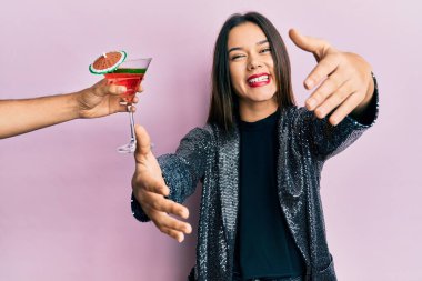 Seksi parti ceketi giyen ve İspanyol kolu olan genç bir kız kameraya bakıp sarılmak için gülümseyen bir kokteyl sunuyor. Mutluluğu kucaklayan neşeli bir ifade.. 