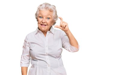 Yaşlı, gri saçlı, günlük kıyafetler giyen, gülümseyen, kendine güvenen, el hareketleriyle küçük beden işareti yapan, parmaklarını gösterip kameraya bakan bir kadın. ölçüm kavramı. 