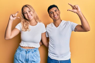 Irklar arası genç bir çift, günlük beyaz tişörtler giyip gülümsüyor ve el hareketleriyle küçük boy işareti yaparak kameraya bakıyor. ölçüm kavramı. 