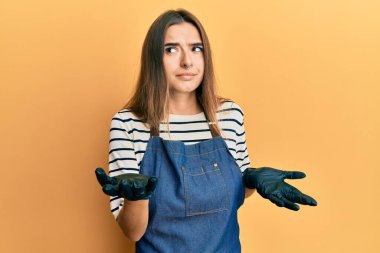 Berber önlüğü takan genç İspanyol kadın, elleri ve kolları havada, kafası karışık bir ifade takınıyor. şüphe kavramı. 