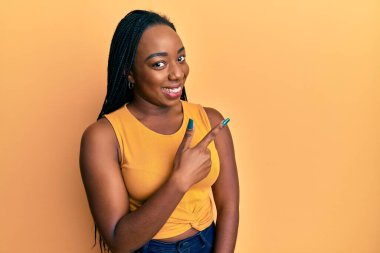 Genç Afro-Amerikan kadın günlük giysiler giyiyor. Neşeli. Yüzünde mutlu ve doğal bir ifadeyle, elleri ve parmaklarıyla yüzünü gösteren bir gülümseme. 