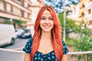 Genç kızıl saçlı kız gülümsüyor Mutlu bir şekilde yürüyor şehrin caddesinde.