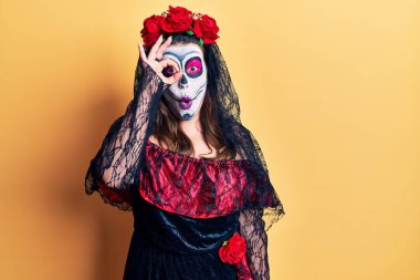 Sarı üzerine ölü kostümü giymiş genç bir kadın şaşırmış yüz ifadesiyle şaşırmış, parmaklarının arasından bakan bir jest yapıyor. İnançsız ifade. 