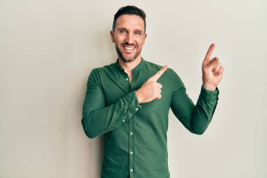 Sakallı, sıradan giyinmiş, gülümseyen ve kameraya bakan yakışıklı bir adam.. 