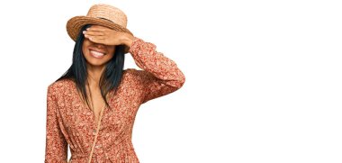 Genç Afro-Amerikan kadın yaz şapkası takıyor. Gülümsüyor ve elleri yüzünde gülüyor. Şaşırtmak için gözleri örtüyor. kör kavram. 