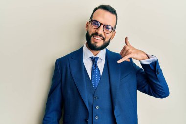 Sakallı, takım elbiseli, kravatlı, gülümseyen, el ve parmaklarıyla telefonla konuşan genç bir adam. iletişim kavramları. 