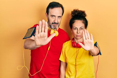 Orta yaşlı bir çift İspanyol kadın ve spor kıyafetleri ve kol bandı takan erkek avuç içiyle şarkı söylemeyi kesiyorlar. Yüzünde olumsuz ve ciddi bir jest olan uyarı ifadesi. 